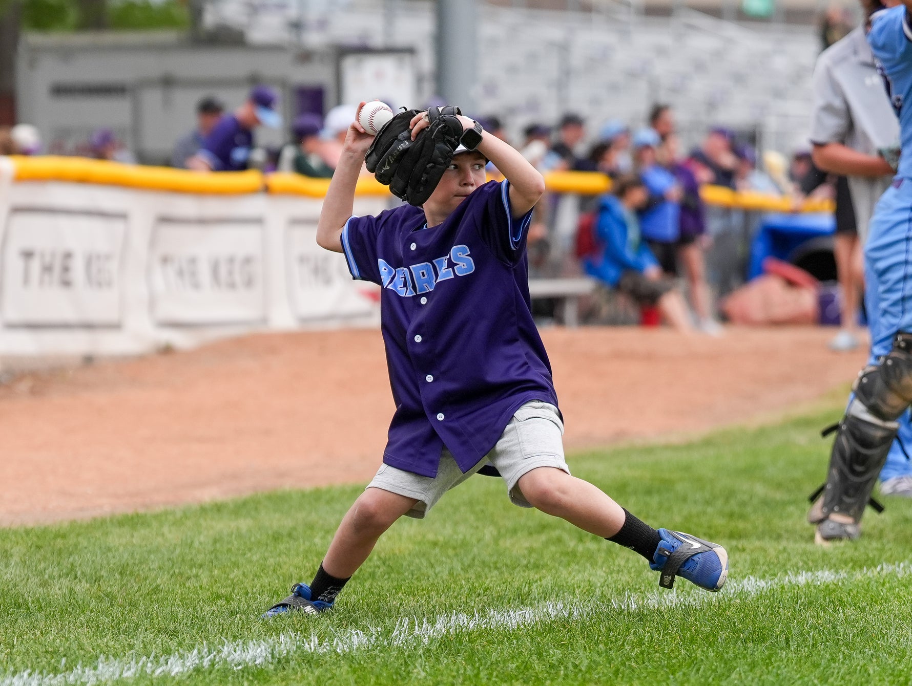 Child in a purple baseball uniform preparing to throw a ball on a baseball field.